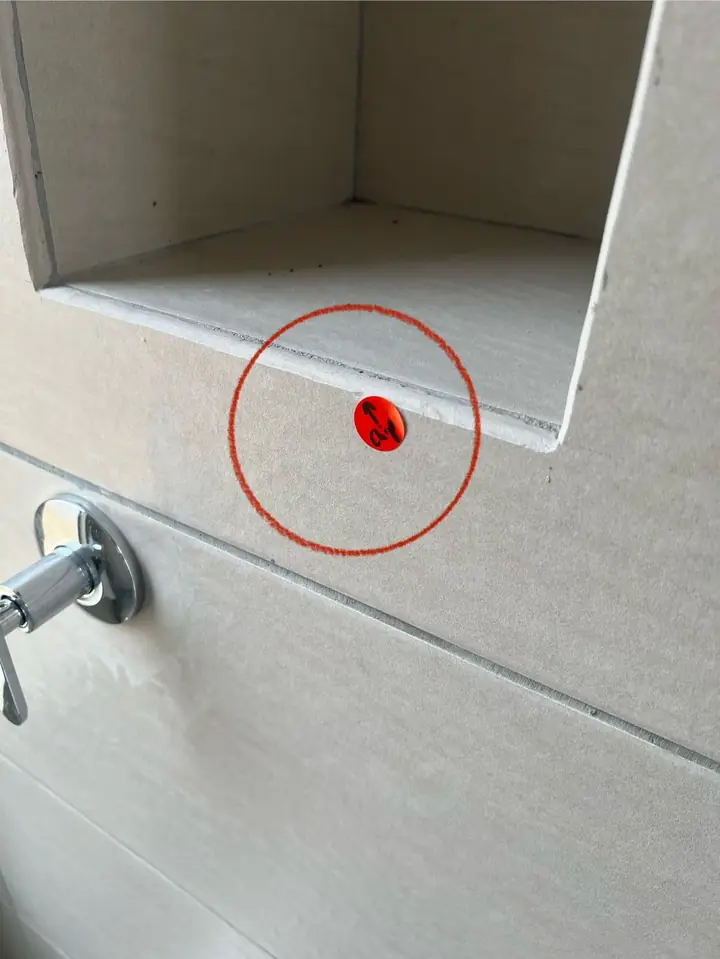 Chipped tile at the edge of a bathroom wall niche, marked with a red sticker