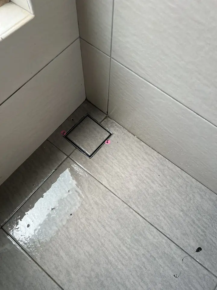Gaps around a bathroom floor trap, marked with pink stickers