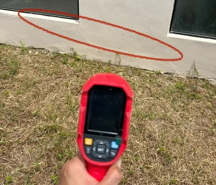 Handheld thermal imager held up to a suspected seepage line on an external wall, circled in red